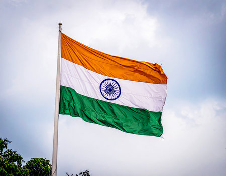 Indian national flag waving in the sky. The tricolor flag features saffron, white, and green horizontal stripes with the blue Ashoka Chakra wheel in the center. Symbol of patriotism, unity, and Indianの素材