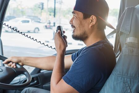 An Asian male truck driver is driving down the road with caution. He is using radio to communicate...