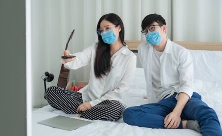 Asian men and women are happily at home. They are using laptops, working and watching news and other TV programs. Staying safe Keep yourself away from society Preventing Covid-19 Infectionの写真素材