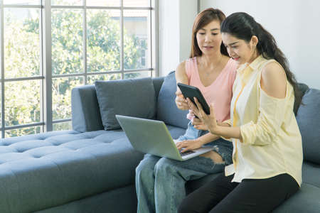 Two attractive Asian women are talking at home happily. Freelance women share casual wear, meetings,...