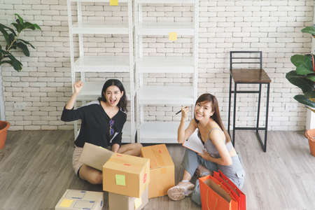Merchant Two attractive young Asian women make living selling products online. They are checking the boxes to send customers. They use communication technology and the internet to marketの写真素材