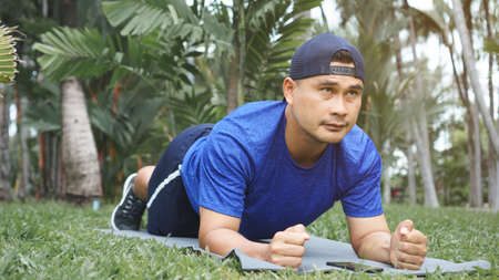 Mature Asian man fit and plank exercise on the grass in the park. sportsman wearing sportswear,...