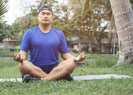 Sportsman meditate on the grass in the park. Young Asian men are healthy and fit to wear sportswear....