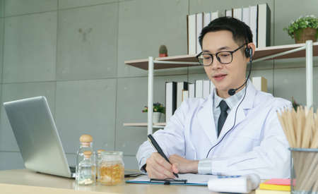 Asian male doctor is using a laptop computer to connect to the internet for online counseling. The medical profession, technology, communication, distance, and people conceptの写真素材