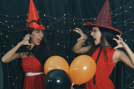 Beautiful woman and friend in Halloween devil costume and wearing witch hat. Have fun at nightclub party, decorate the lights by doing a scary face. Halloween celebrationの写真素材