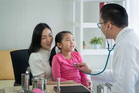 Happy Asian, adult mother and childhood daughter, checkup at the clinic.  pediatrician, listen to preschool girls' heartbeat. Male doctor, consultation and guidance of kid patientsの写真素材