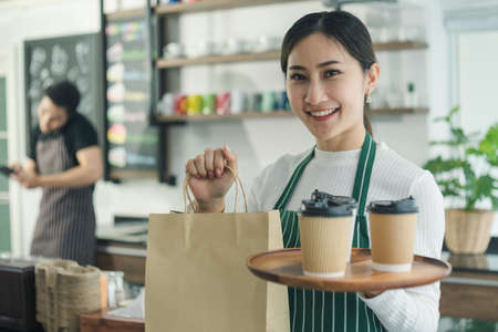 Attractive young Asian woman smiling confident in cafe. young female barista, owner coffee shop,...