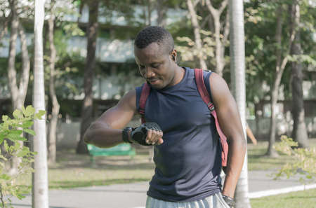 African American male sportsman exercise outdoor. African man athletes Sports training in park. young, muscular black man, smiling and relaxed looking at his wristwatch. Health and fitness concept.の写真素材