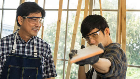 Two Asian carpenters working together in workspace. mature adult father and growing son preparing...