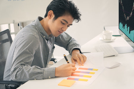 Young male trader analysis forex stock chart on desktop computer screen in modern office. man new generation financier making accounts Currency exchange and trading rates in the stock market.の写真素材