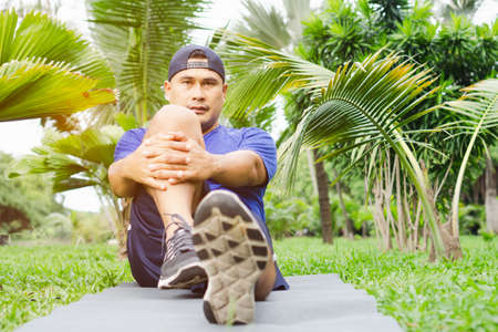 Fat man in sportswear exercising relaxing in garden. healthy young male sitting stretching...