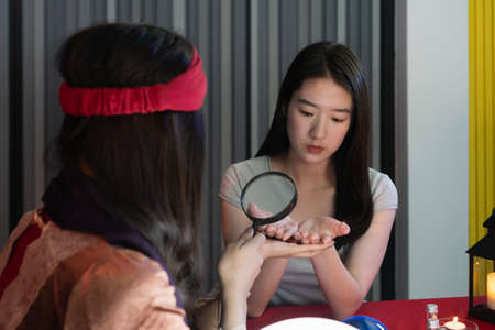 Attractive beautiful Asian woman hands to fortune teller Use a magnifying glass to read the lines of...