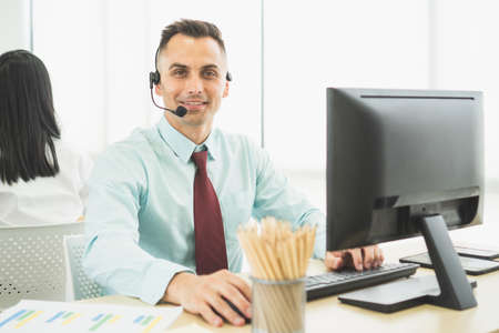 portrait call center male smiling confident positive friendly wear headset desktop computer incoming calls talk service support customer. Concept, operator, sales, telemarketing, online assistant.の写真素材