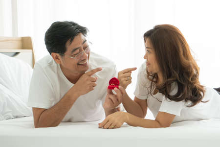Happy Mature Couple Relax At Home Vacation. Romantic middle-aged husband giving gift gold ring his wife dear on valentine's day. senior man woman retirement healthy living together with family warm.の写真素材