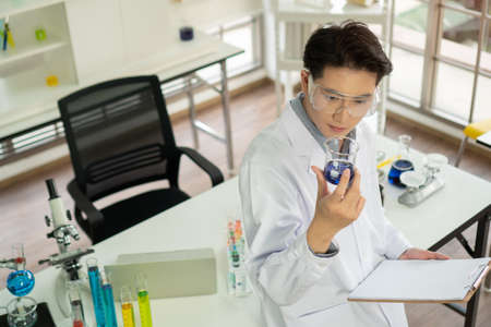 portrait Asian Man Researcher smiling confident Holding Test Tube in modern lab. male Scientists science experiment with biological chemistry in laboratory high safety Analyze results and take notes.の写真素材