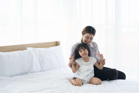 portrait little daughter playful togetherness with young mother in bedroom comfortable morning vacation. Asian family happy have fun parents take care of children.の写真素材