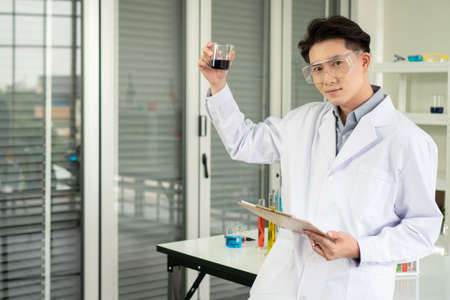 portrait Asian Man Researcher smiling confident Holding Test Tube in modern lab. male Scientists science experiment with biological chemistry in laboratory high safety Analyze results and take notes.の写真素材