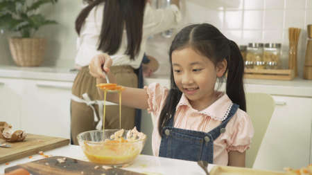 happy Asian family. young mother, and daughter little prepare dinner healthy food in modern kitchen. Cute girl playful learning to bake bread having fun Her Mixing food recipes.の写真素材