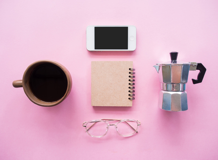 Creative flat lay photo of coffee workspace with coffee maker, coffee grinder, black coffee, glasses, notebook and smartphone on pink background  with copy space, minimal style.の写真素材