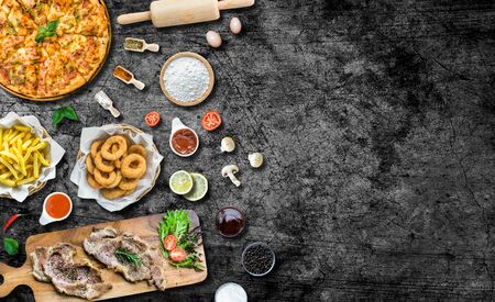 Flat lay italian pizza and grilled beef steak on wooden cutting board and ingredient. Crispy Onion rings and french fries. tomato and chili sauce. Top view with copy spaceの写真素材