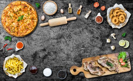 Flat lay italian pizza and grilled beef steak on wooden cutting board and ingredient. Crispy Onion rings and french fries. tomato and chili sauce. Top view with copy spaceの写真素材
