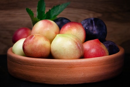 plums and nectarines on clay plate on wooden background with mintの写真素材