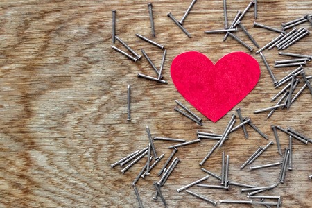 Red love heart on wooden background surrounded by iron nailsの写真素材