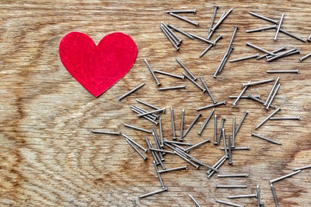 Red love heart on wooden background surrounded by iron nailsの写真素材