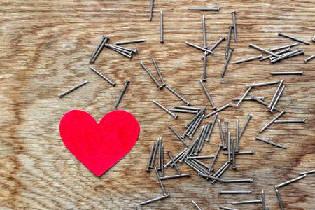 Red love heart on wooden background surrounded by iron nailsの写真素材