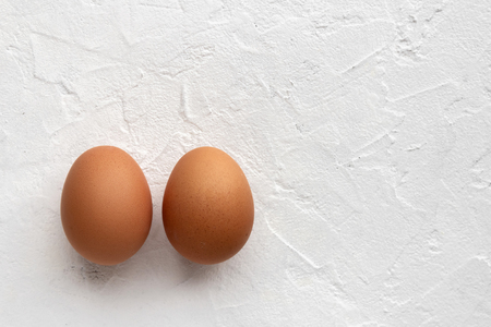 Two fresh eggs on white textural background with egg's shadow and copy spaceの写真素材