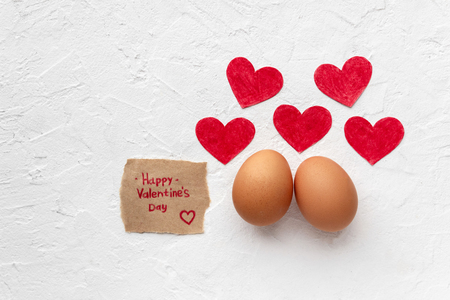 Two fresh eggs with five red loving paper hearts lie on white textural background with egg's shadow for Valentines day concept with copy spaceの写真素材