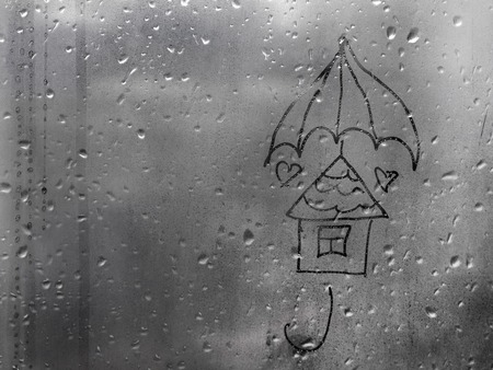 drawn house under an umbrella on a wet window with copy spaceの写真素材