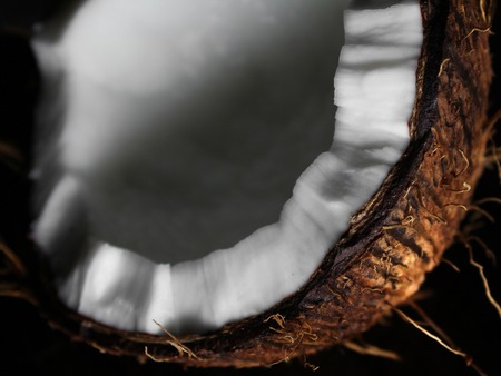 one half of chopped fresh coconut with shadows on a dark background