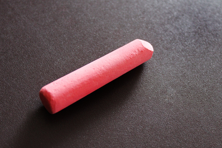 a piece of pink chalk lies on a brown background of a magnetic board and casts a shadowの写真素材