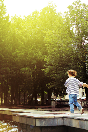 charming happy little child in the sunlight walks in the park in the summer, his hand is held so as not to fallの写真素材
