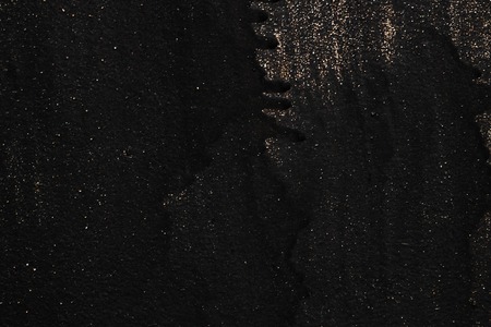 The metal texture of the background painted in black paint with smudges, scratches and splashes of gold sparkles, copy spaceの写真素材