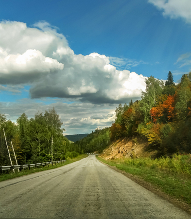 asphalt road goes into the distance in nature with a beautiful landscape and clouds in the blue skyの写真素材