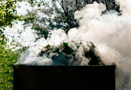 beautiful puffs of sunlight in the sun burning grass in the garden in an old barrel, the concept of...