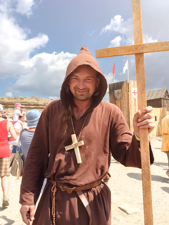 Sudak, Russia - August 16, 2015: man dressed as medieval priest, a monk with a wooden cross with a staff in his hand and with a wooden cross on his neck among the modern crowd at a festival of historical reconstructionのeditorial素材