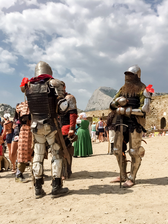 Sudak, Russia - August 16, 2015: two medieval knights in armor, armor, chain mail and helmets during the festival stand against the background of mountains, fortress walls and crowds of spectatorsのeditorial素材