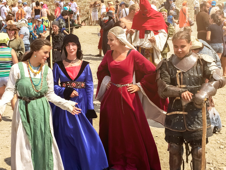 Sudak, Russia - August 16, 2015: three girls in dresses of medieval ladies and a man in the armor of a medieval knight are chatting amid a crowd of spectators at a historic festivalのeditorial素材