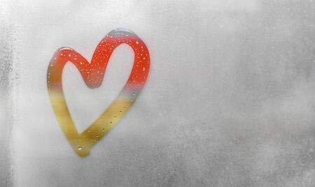 Red and orange heart painted on sweaty glass, there are many drops on it, inscription heart and love on a wet autumn foggy glass. valentines day concept with copy space for textの写真素材