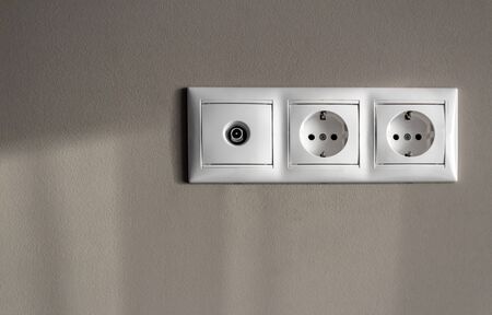 electrical outlets, set of three white empty electrical sockets for appliances and antenna socket for TV with light shadow on empty grey background, electrical point of power in house, closeup, minimalism conceptの写真素材