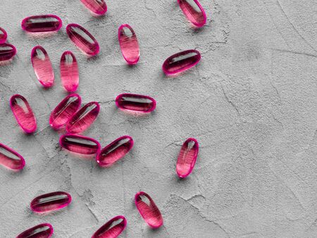 Several pink soft gelatin transparent capsules laid out on a gray concrete background with copy space . The concept of pharmacologyの写真素材