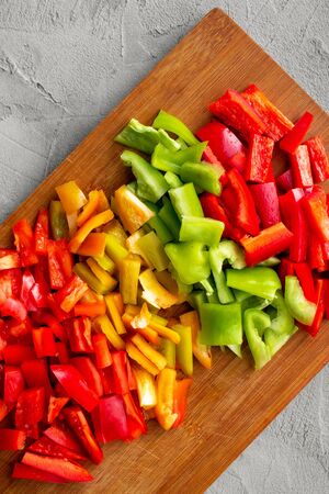 colorful chopped bell peppers - red, yellow, green - cut in cubes on wooden board on gray concrete, autumn cooking lecho, flat layの写真素材