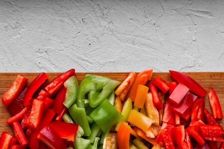 colorful chopped bell peppers - red, yellow, green - cut in cubes on wooden board on gray concrete, autumn cooking lecho, flat layの写真素材