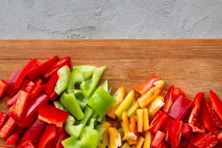 colorful chopped bell peppers - red, yellow, green - cut in cubes on wooden board on gray concrete, autumn cooking lecho, flat layの写真素材