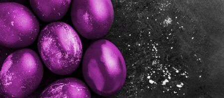 Greeting card with easter eggs painted in fluorescent glowing purple color on black background with white crumbs, egg shell with white stains, scuffs, scratches. handmade painted eggs. Flat lay with copy space, top viewの写真素材