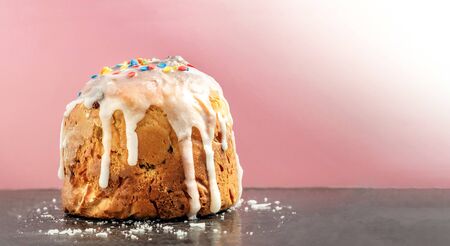 Homemade easter cakes with icing and colored confetti close-up standing on a black surface with icing crumbs on a pink background. Morning baking, easter card with copy spaceの写真素材