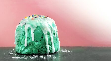 Homemade easter cakes painted in Aqua Menthe with icing and colored confetti close-up standing on a black surface with icing crumbs on a pink background. Morning baking, easter card with copy spaceの写真素材